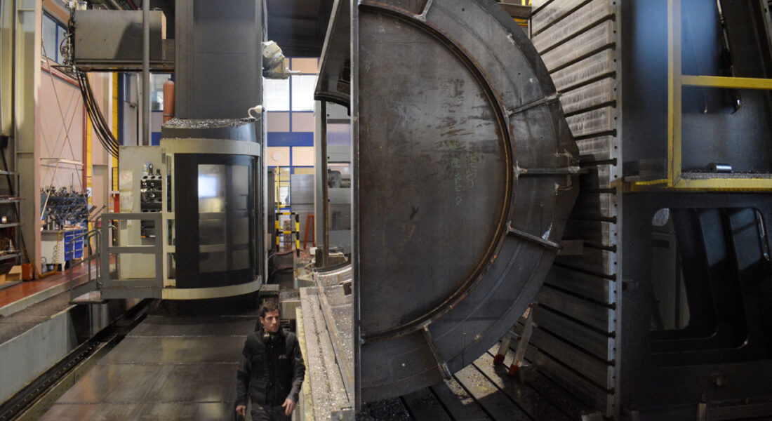 Operario revisando la instalación de estructura de horno de grandes dimensiones preparada para ser mecanizada en la fresadora Zayer Kairos 12000. A la izquierda, la cabina de la fresadora. Vista lateral. La estructura es 3 veces la altura del operario